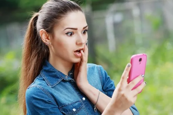 Девушка удивленно смотрит на экран своего смартфона 